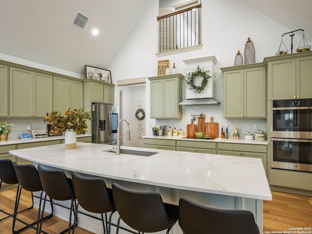 kitchen with visible vents, a breakfast bar, a sink, stainless steel appliances, and green cabinets