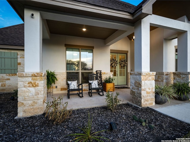 entrance to property featuring french doors, stone siding, roof with shingles, and stucco siding