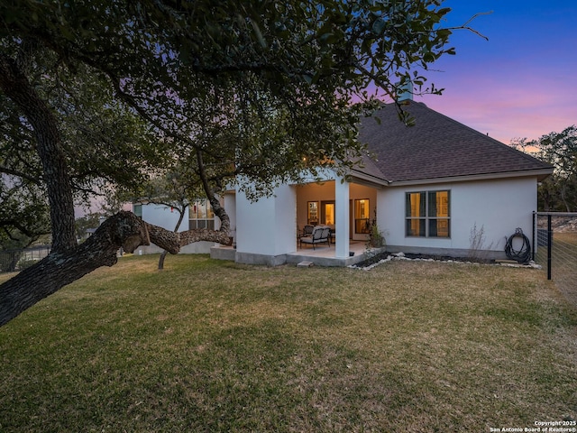 rear view of house with stucco siding, fence, a yard, roof with shingles, and a patio area