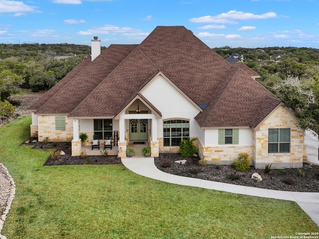 view of front facade featuring a front lawn, stone siding, roof with shingles, and a chimney