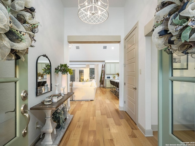 corridor featuring a high ceiling, visible vents, light wood-style floors, and an inviting chandelier