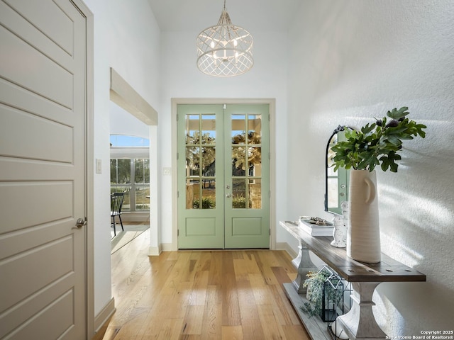 doorway to outside featuring french doors, baseboards, light wood-type flooring, and an inviting chandelier