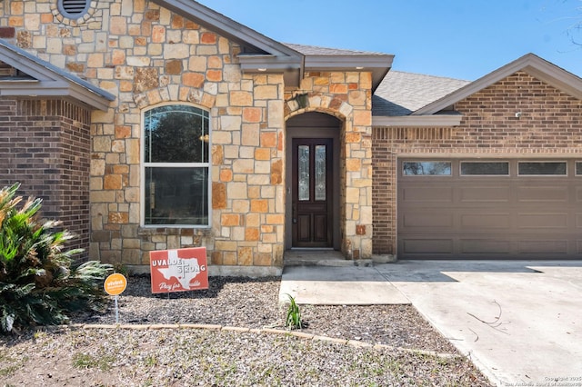 entrance to property with stone siding, roof with shingles, concrete driveway, and an attached garage