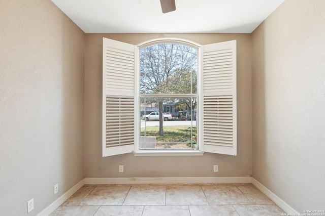 empty room featuring light tile patterned floors, a ceiling fan, and baseboards