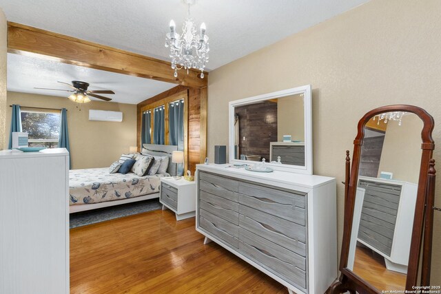 bedroom featuring a wall mounted air conditioner, a textured ceiling, wood finished floors, and ceiling fan with notable chandelier