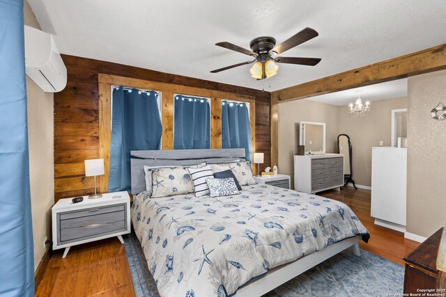 bedroom featuring wood finished floors, baseboards, an AC wall unit, a textured ceiling, and a notable chandelier