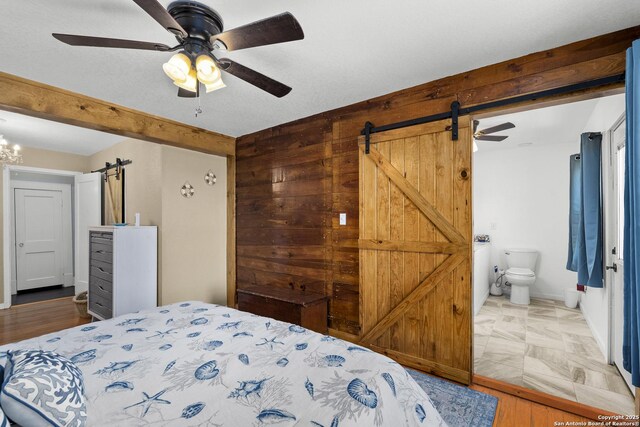 bedroom with ensuite bathroom, ceiling fan with notable chandelier, a textured ceiling, a barn door, and wood walls