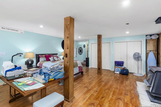 bedroom with a wood stove, recessed lighting, multiple closets, and light wood finished floors