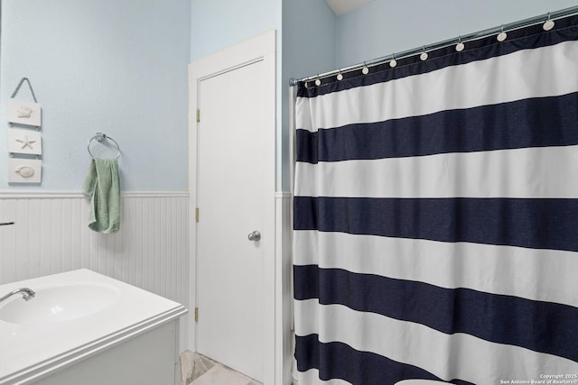 full bathroom featuring a shower with shower curtain, a wainscoted wall, and vanity