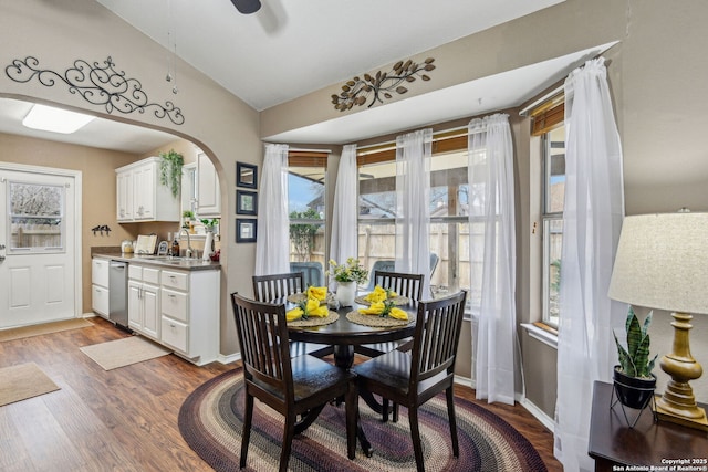 dining space featuring arched walkways, wood finished floors, baseboards, and vaulted ceiling