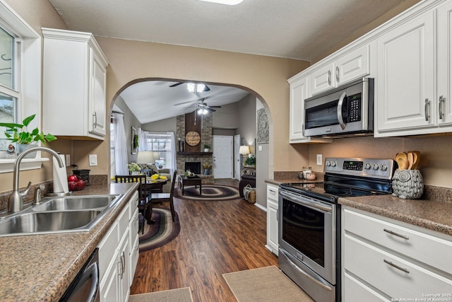 kitchen with a ceiling fan, a sink, stainless steel appliances, white cabinetry, and a large fireplace