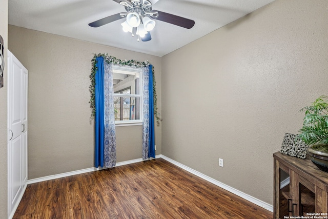 unfurnished room with a ceiling fan, baseboards, dark wood-style flooring, and a textured wall