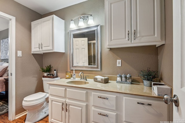 bathroom with wood finished floors, toilet, vanity, and a textured wall