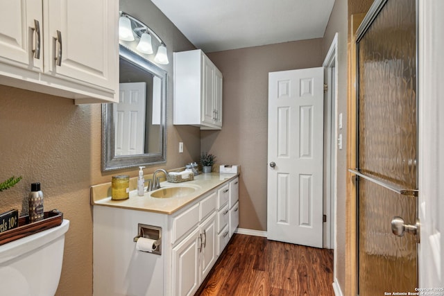 bathroom with toilet, wood finished floors, baseboards, vanity, and a textured wall