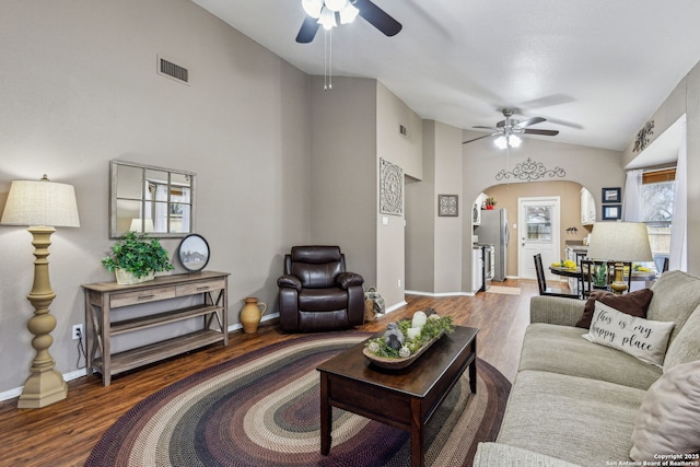 living room featuring wood finished floors, visible vents, lofted ceiling, arched walkways, and ceiling fan