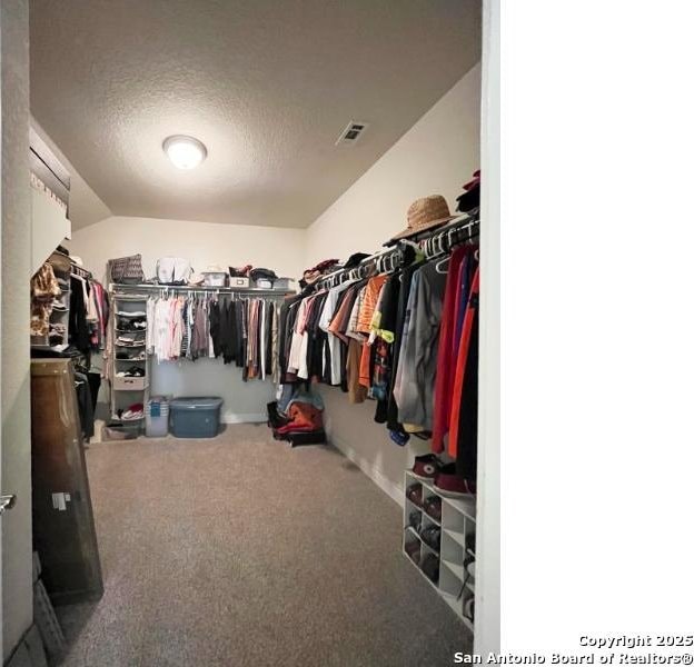 spacious closet featuring lofted ceiling, carpet flooring, and visible vents