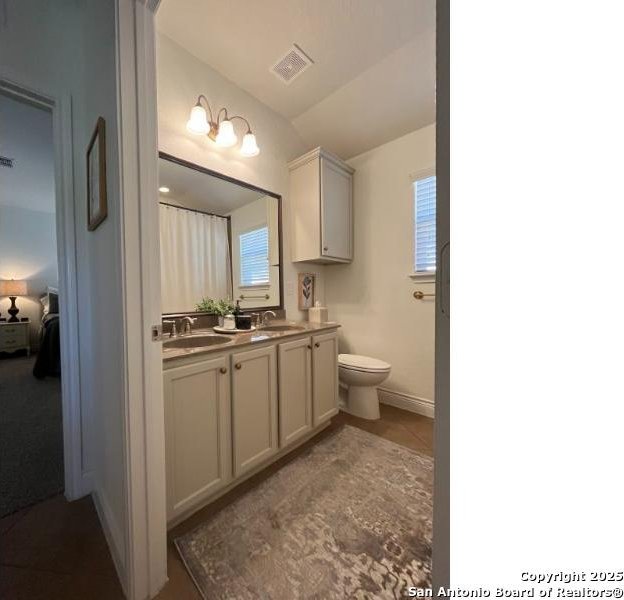 bathroom with double vanity, visible vents, toilet, and a sink