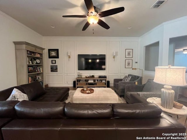 living room with a decorative wall, a ceiling fan, visible vents, and ornamental molding