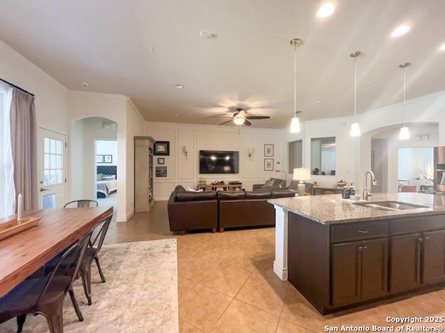 kitchen featuring light stone countertops, dark brown cabinetry, light tile patterned flooring, arched walkways, and a sink