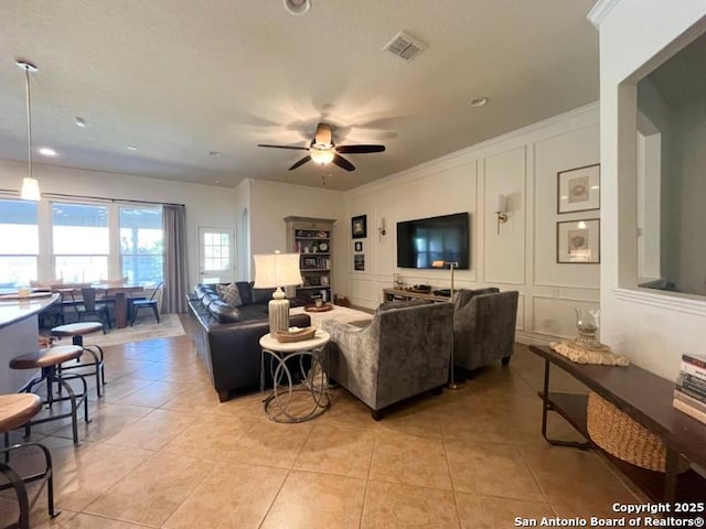 living room with visible vents, ceiling fan, ornamental molding, light tile patterned flooring, and a decorative wall