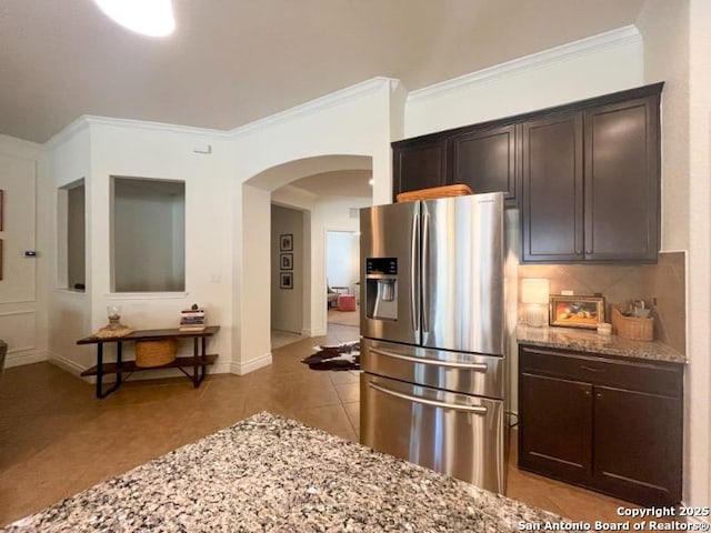 kitchen featuring light stone countertops, light tile patterned flooring, decorative backsplash, dark brown cabinetry, and stainless steel fridge