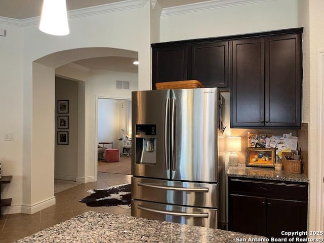 kitchen featuring visible vents, dark stone countertops, arched walkways, light tile patterned flooring, and stainless steel fridge with ice dispenser