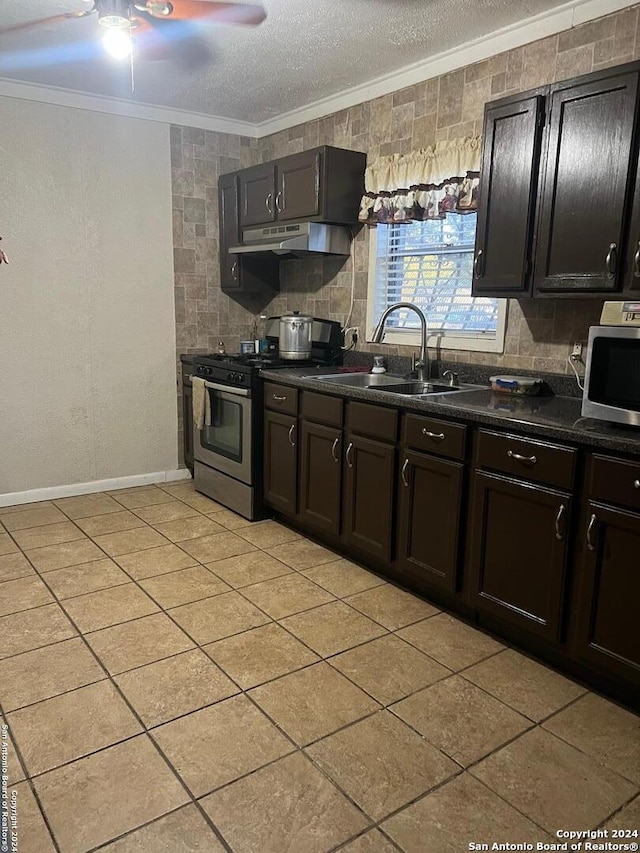 kitchen with dark countertops, crown molding, under cabinet range hood, appliances with stainless steel finishes, and a sink