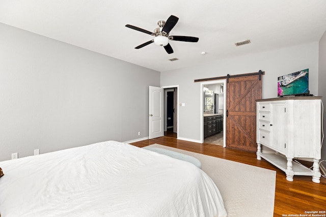 bedroom featuring a barn door, wood finished floors, visible vents, and baseboards