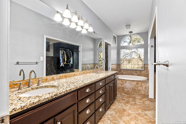 full bathroom with a walk in closet, double vanity, tiled tub, and a sink