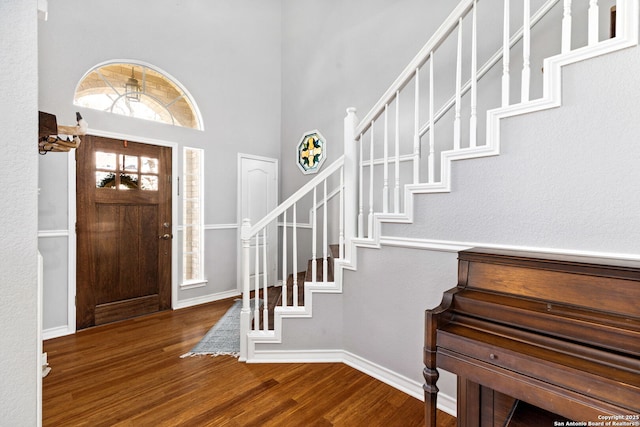 entryway with a towering ceiling, stairs, baseboards, and wood finished floors