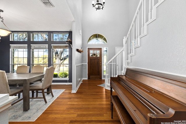 foyer entrance featuring visible vents, dark wood-type flooring, a notable chandelier, a high ceiling, and stairs