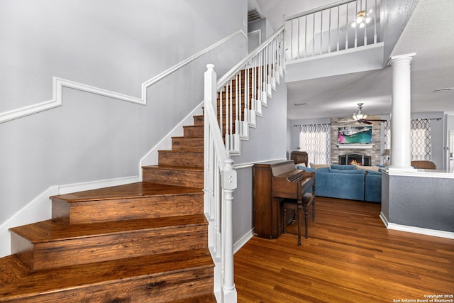 stairs with a ceiling fan, wood finished floors, a fireplace, baseboards, and ornate columns