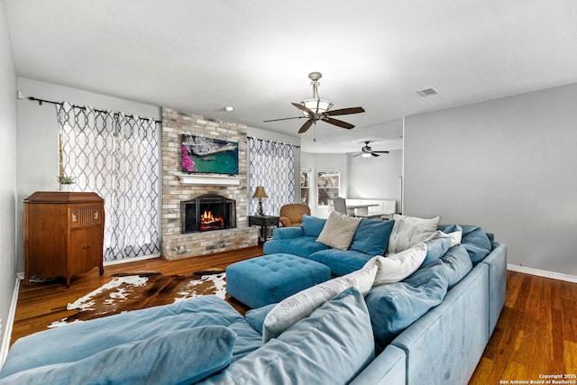 living room featuring dark wood-type flooring, a brick fireplace, visible vents, and baseboards