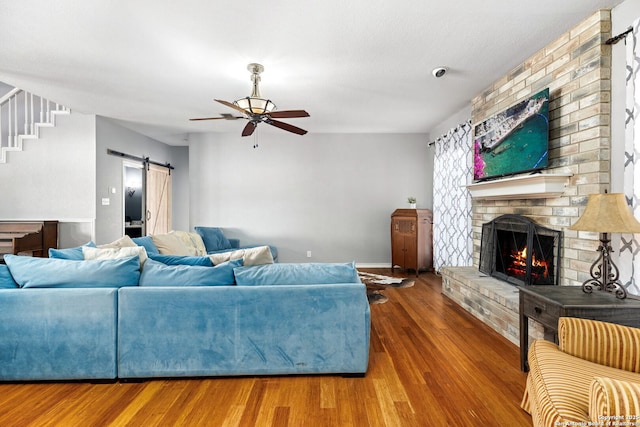 living area featuring stairway, a barn door, a fireplace, wood finished floors, and a ceiling fan