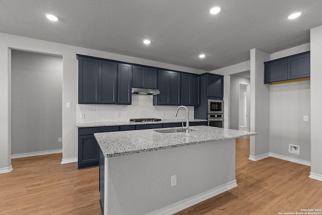 kitchen with light wood-type flooring, a sink, under cabinet range hood, light stone counters, and stainless steel appliances