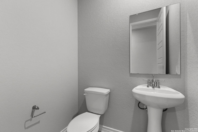 bathroom featuring toilet, a textured wall, and baseboards