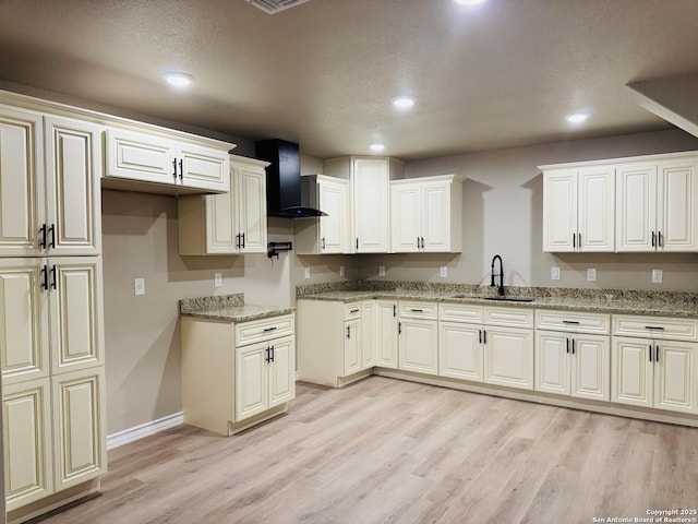 kitchen with light stone countertops, light wood-style flooring, recessed lighting, a sink, and wall chimney range hood