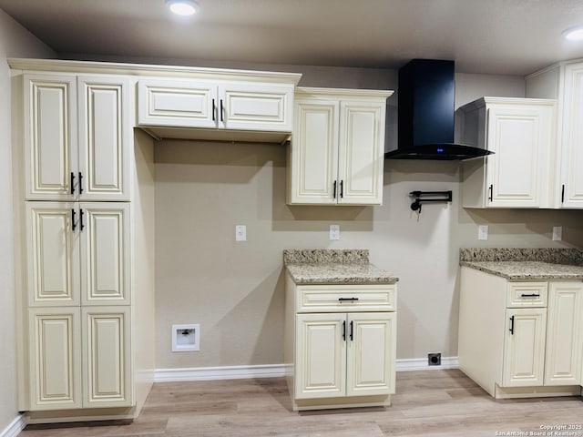 kitchen with baseboards, light stone countertops, wall chimney exhaust hood, and light wood finished floors