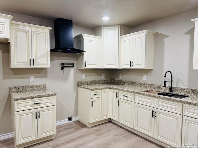 kitchen with baseboards, light stone countertops, wall chimney range hood, light wood-type flooring, and a sink