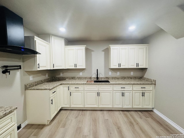 kitchen with wall chimney range hood, light wood-style floors, light stone countertops, and a sink