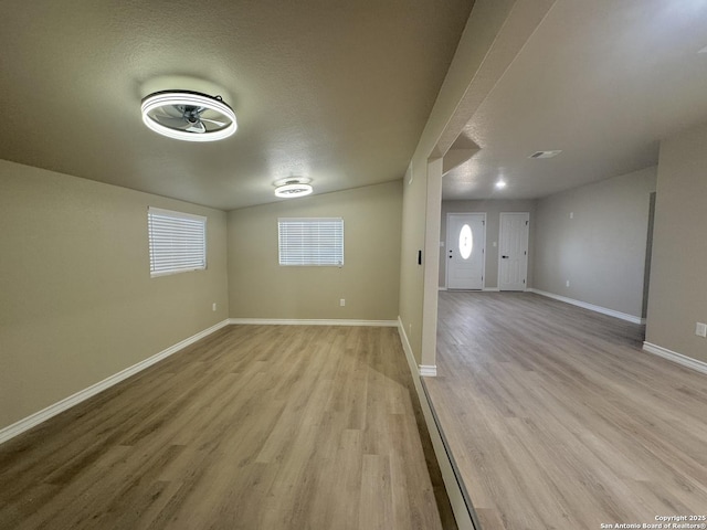 basement featuring visible vents, light wood-style floors, baseboards, and a textured ceiling