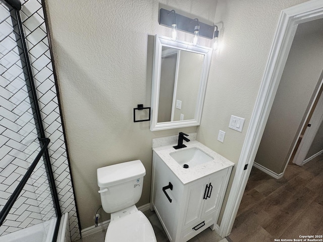 bathroom featuring toilet, wood finished floors, a shower, vanity, and a textured wall