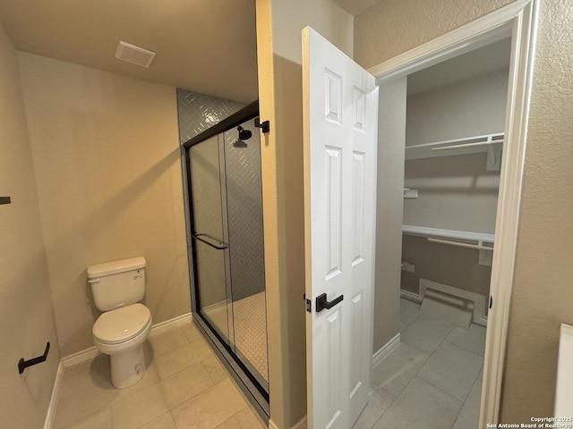 bathroom featuring a walk in closet, tile patterned floors, toilet, and a stall shower