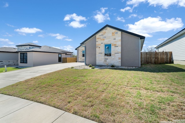 view of front of home with stone siding, concrete driveway, a front yard, and fence