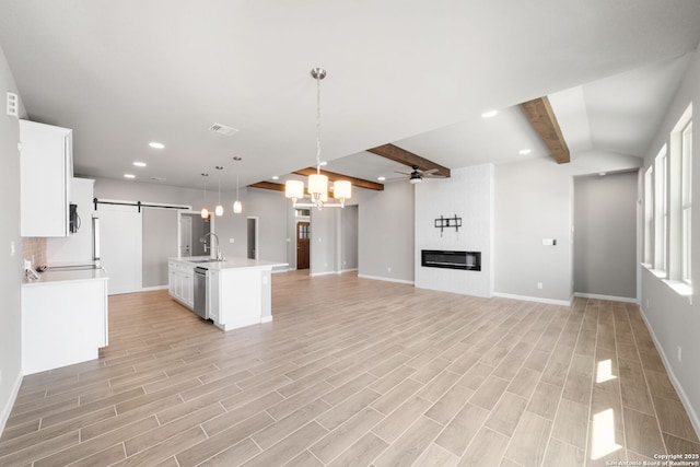 kitchen with ceiling fan with notable chandelier, a sink, a barn door, a large fireplace, and light countertops