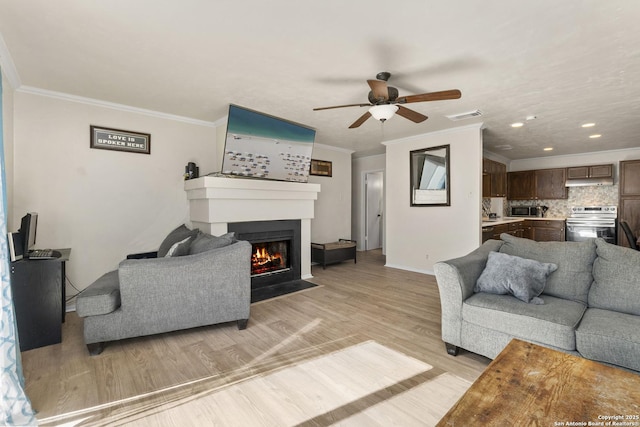 living room featuring visible vents, light wood-style floors, a fireplace with flush hearth, and ornamental molding