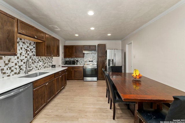 kitchen featuring light wood finished floors, crown molding, under cabinet range hood, stainless steel appliances, and a sink