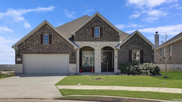 french provincial home with roof with shingles, concrete driveway, a front lawn, stone siding, and brick siding