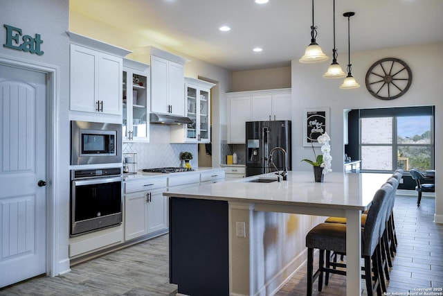 kitchen with a sink, under cabinet range hood, a breakfast bar area, stainless steel appliances, and a kitchen island with sink