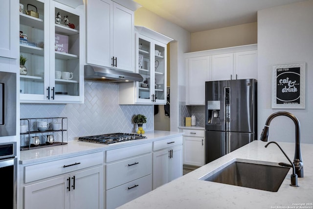 kitchen featuring under cabinet range hood, light stone counters, appliances with stainless steel finishes, white cabinetry, and a sink